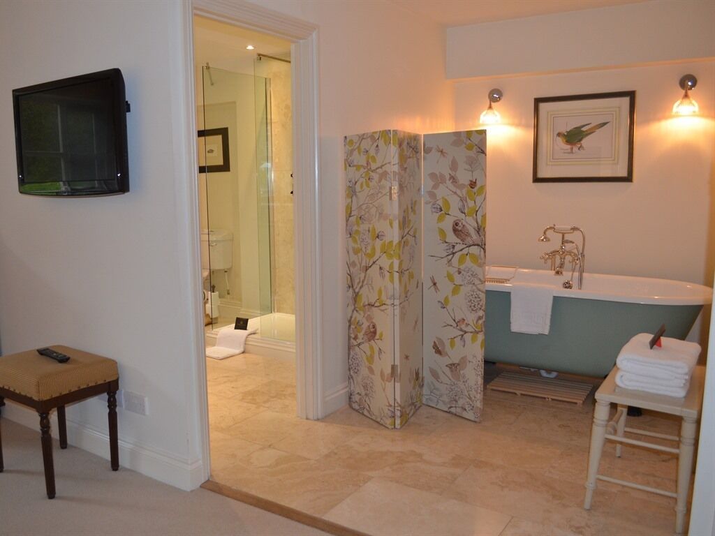 Une salle de bain avec une baignoire, une douche et des toilettes. On y trouve un banc et un porte-serviettes.
