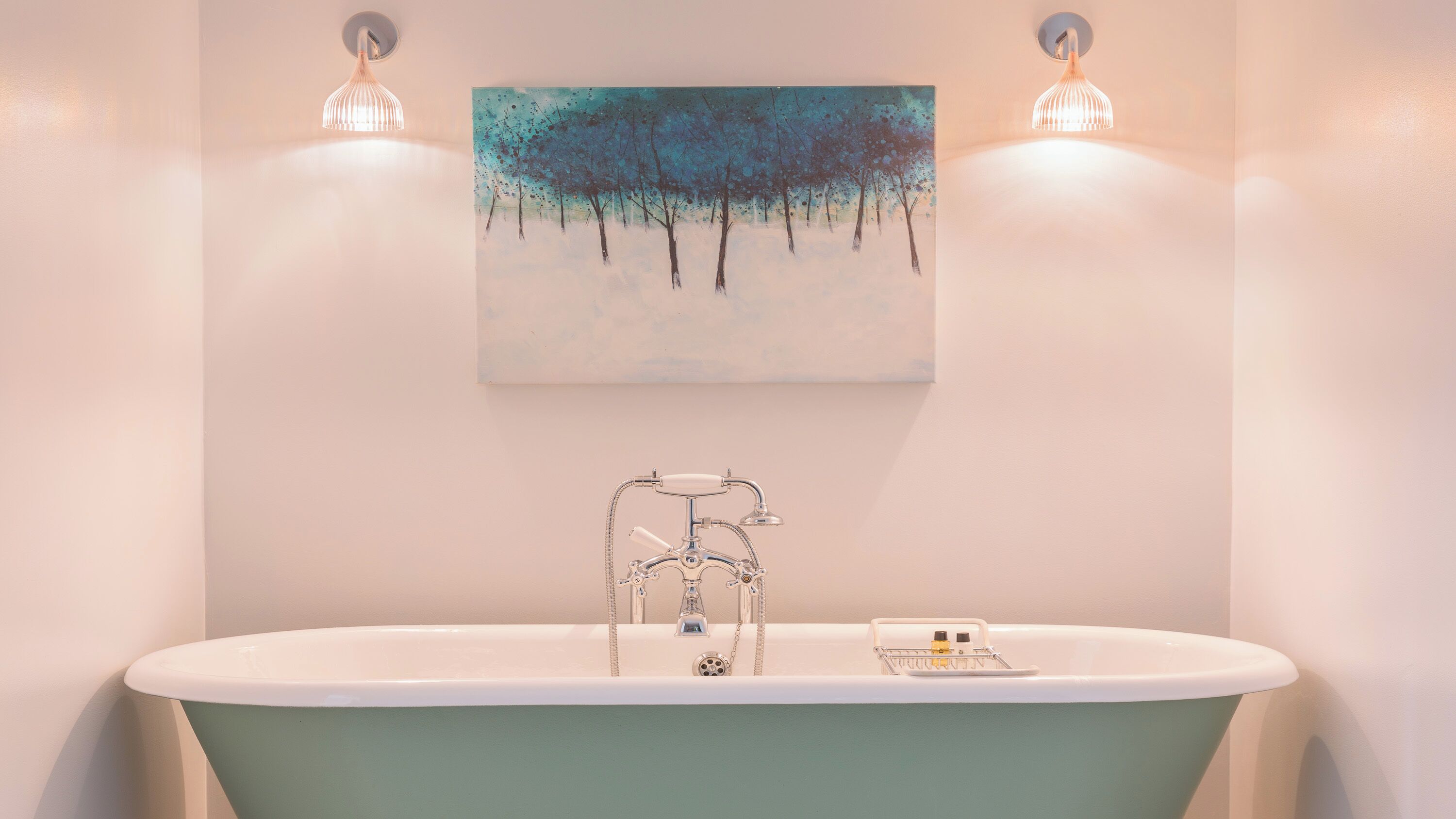 A bathroom with a freestanding bathtub, a wall-mounted painting, and two wall-mounted light fixtures.