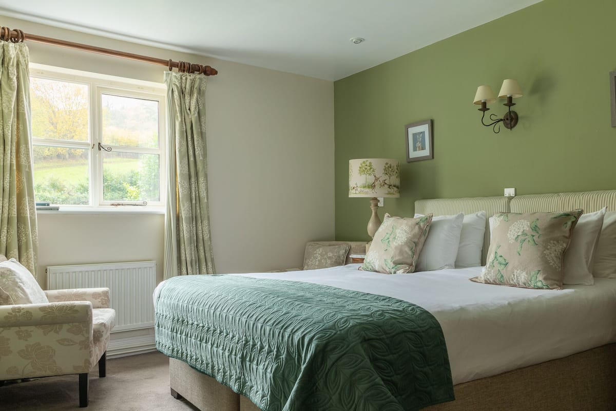 A bedroom with a large bed, a chair, a window with curtains, and wall-mounted lamps.