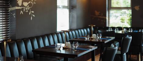 A restaurant interior with dark leather booths, wooden tables, and hanging light fixtures.