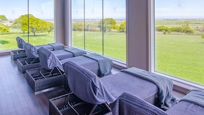 A room with large windows offering a view of a green landscape. There are several wicker chairs with cushions. - The Kinmel & Kinspa (Abergele)