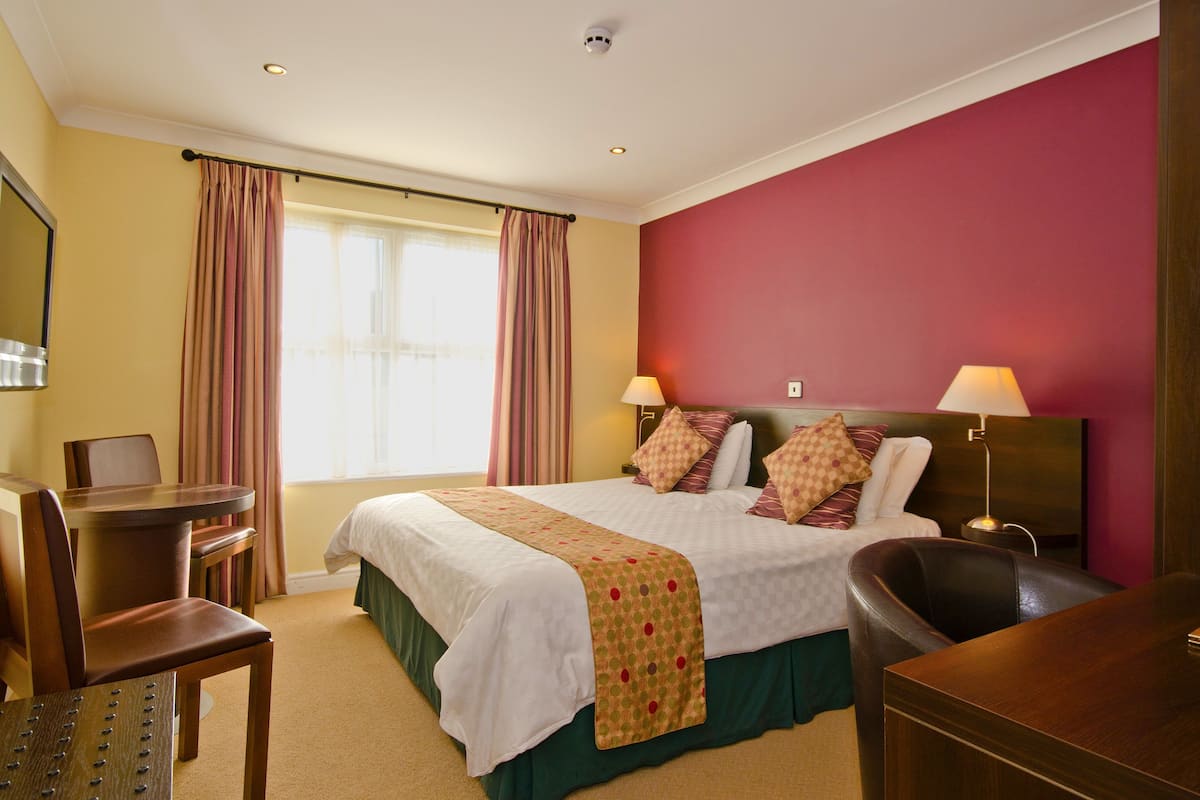 A hotel room with a bed, two bedside lamps, a desk, and a chair.