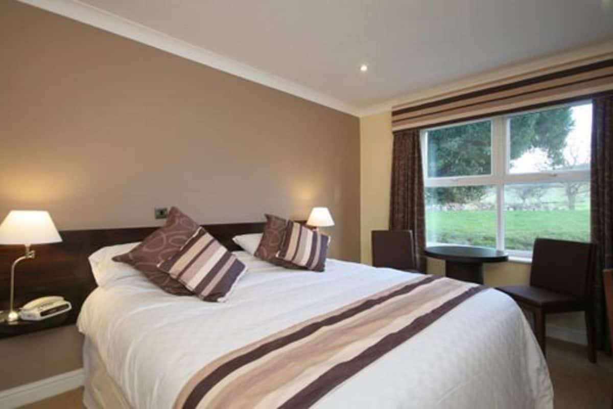 A hotel room with a large bed, two bedside lamps, a window with curtains, and a view of the outdoors.