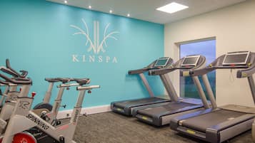 Ein Fitnessstudio mit Spinning-Rädern, Laufbändern und einer blauen Wand mit dem KINSPA-Logo.