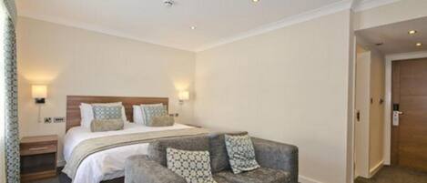 Una camera d'albergo con un letto, un divano grigio e un comodino.
