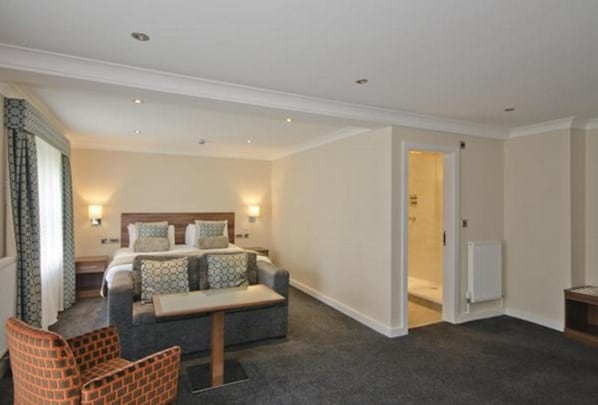 A hotel room with a bed, a sofa, a small table, and a chair. There is a door leading to a bathroom. - The Kinmel & Kinspa (Abergele)