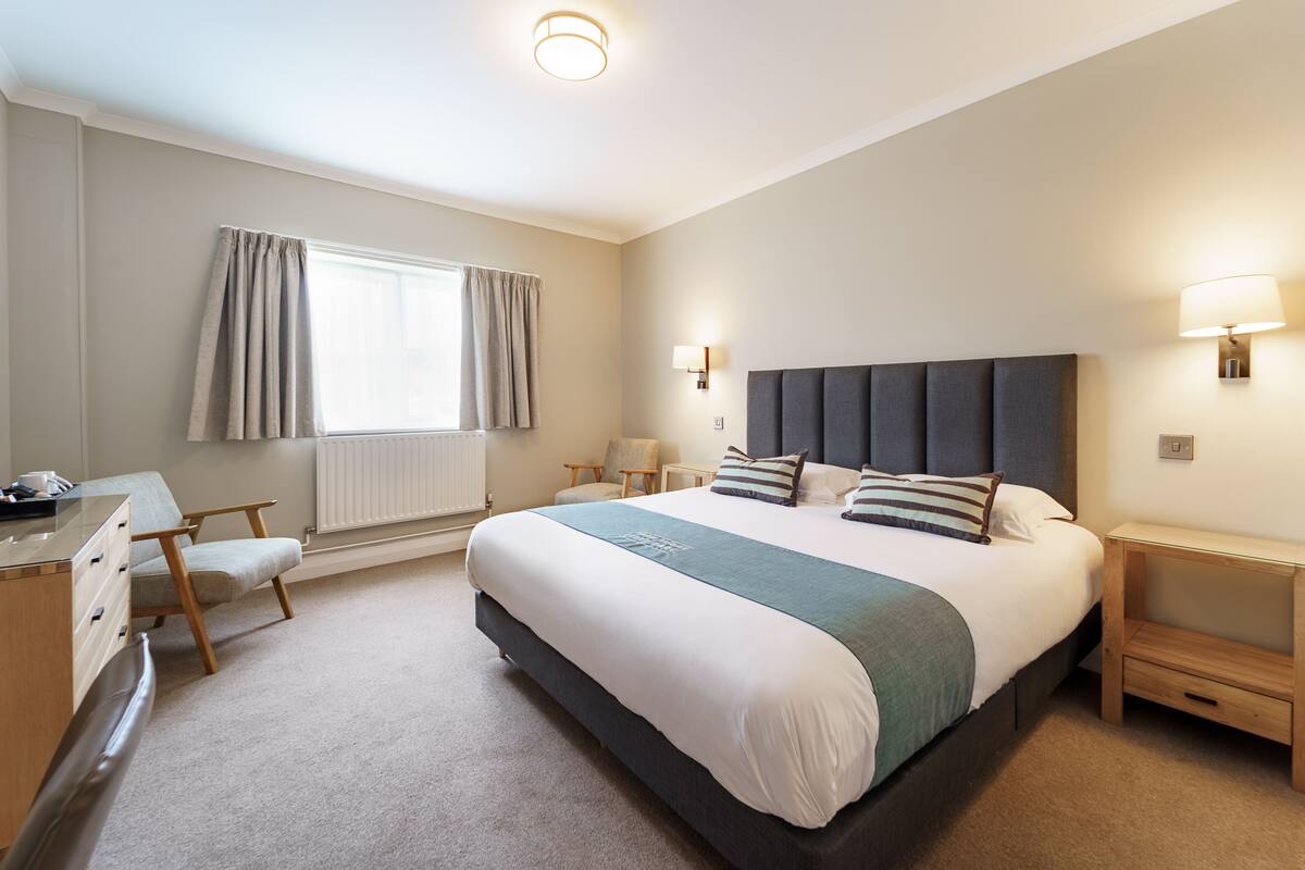 A modern hotel room with a large bed, bedside tables, a desk, and a chair.