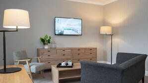 Una habitación moderna con un escritorio de madera, dos sillones, una mesita de centro, un armario y dos lámparas de pie.