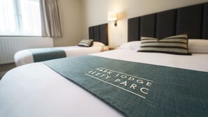 Habitación de hotel con dos camas, cabecero, lámpara de noche y ventana con cortinas.