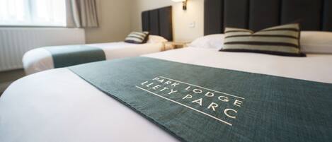 A hotel room with two beds, a headboard, a bedside lamp, and a window with curtains.