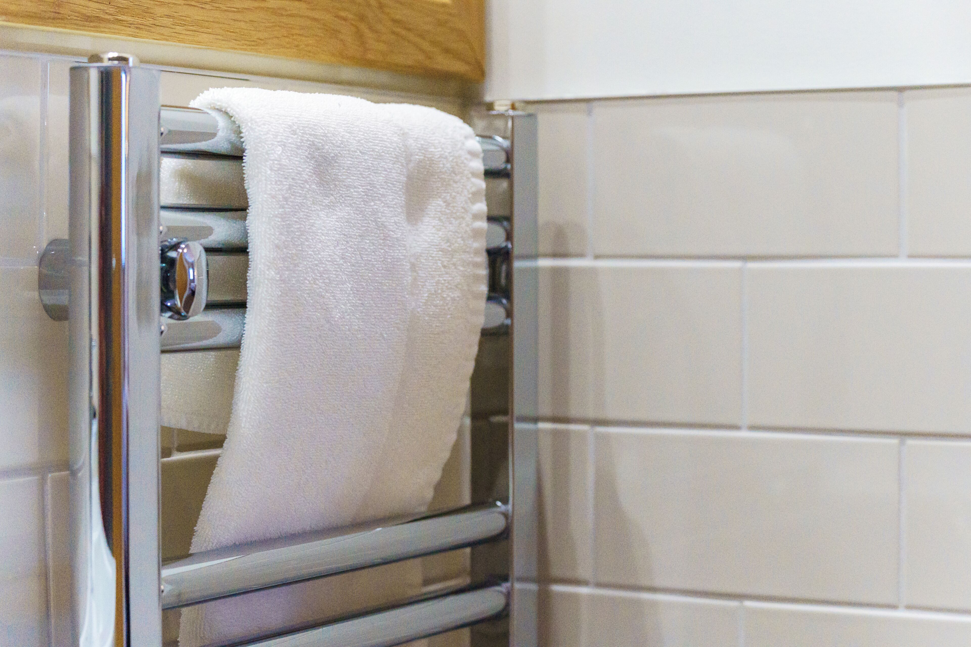 A towel rack with a white towel hanging on it, a metallic handle, and a tiled wall in the background.