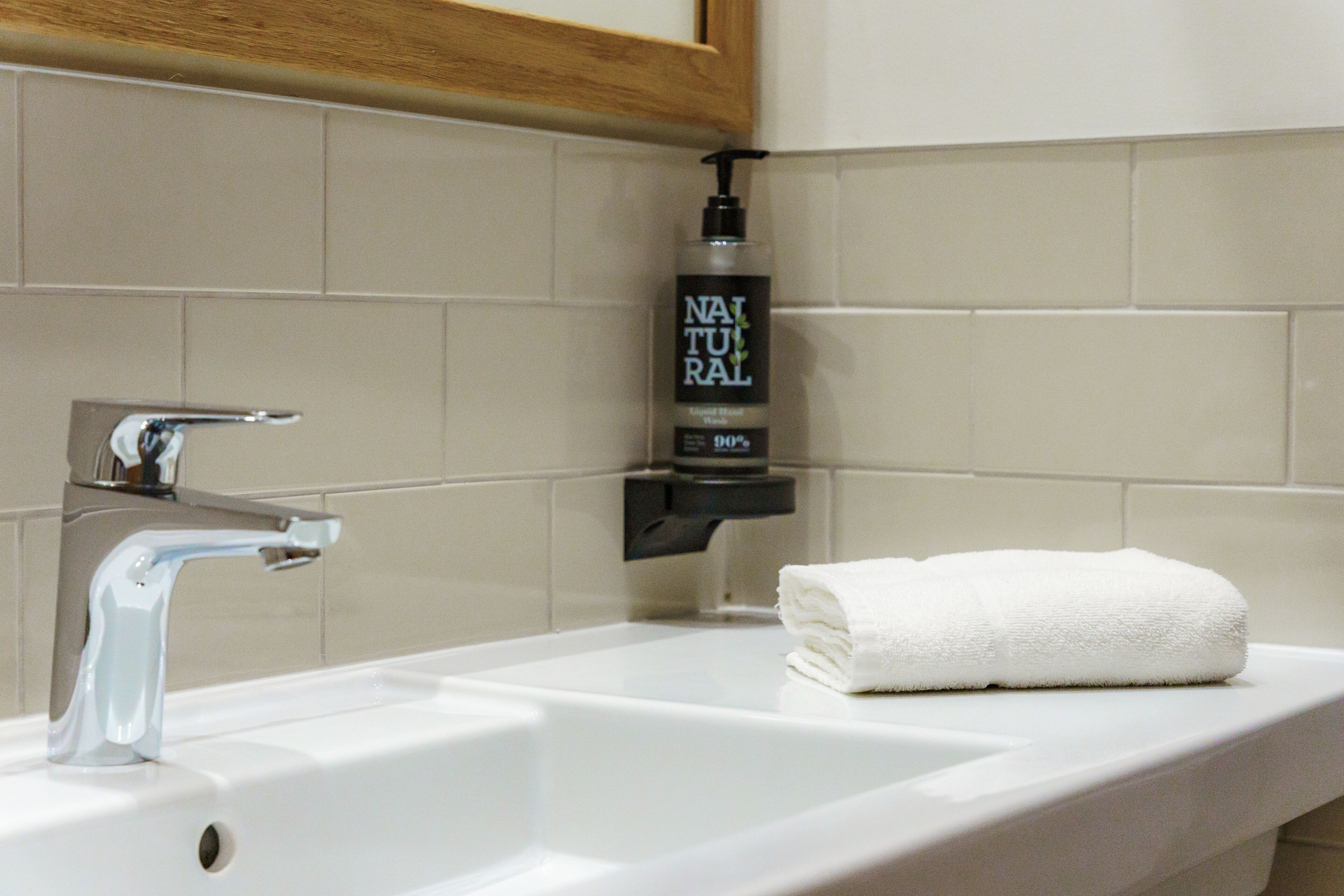 A bathroom with a white sink, a faucet, and a bottle of shampoo.