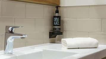 A bathroom with a white sink, a faucet, and a bottle of shampoo.
