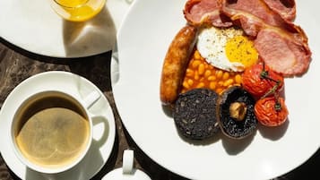 Een ontbijt bord met spek, eieren, bonen, tomaten en bloedworst, vergezeld van een kop koffie en een glas jus d'orange.
