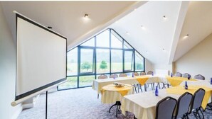 Un salón de conferencias con una gran mesa, sillas, una pantalla de proyector y vistas al exterior a través de amplias ventanas.