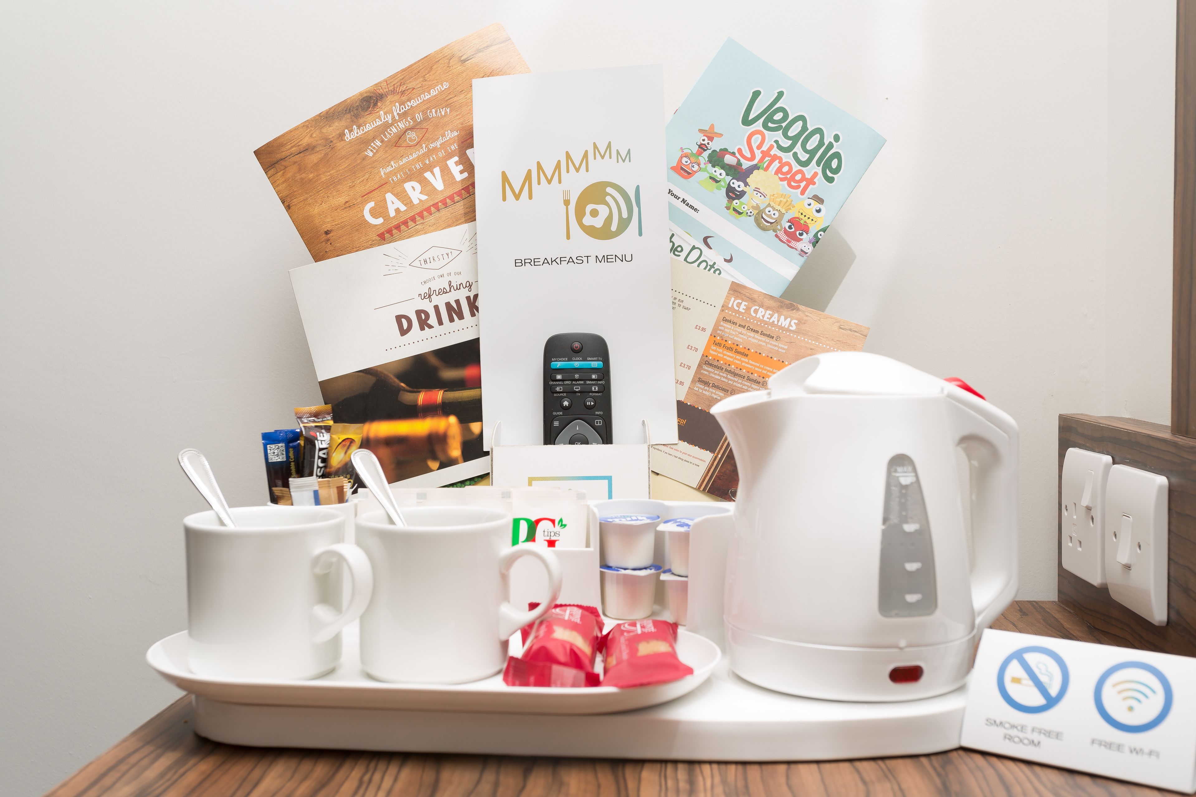A breakfast setup with coffee cups, a kettle, and various breakfast items on a tray.