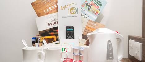 A breakfast setup with coffee cups, a kettle, and various breakfast items on a tray.