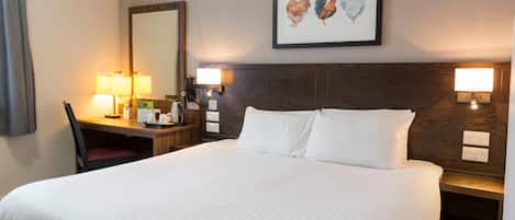 A hotel room with a large bed, a desk with a chair, two bedside lamps, and a framed picture on the wall.
