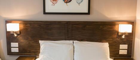 A hotel room with a large bed, two bedside tables, and a framed artwork of chickens on the wall.