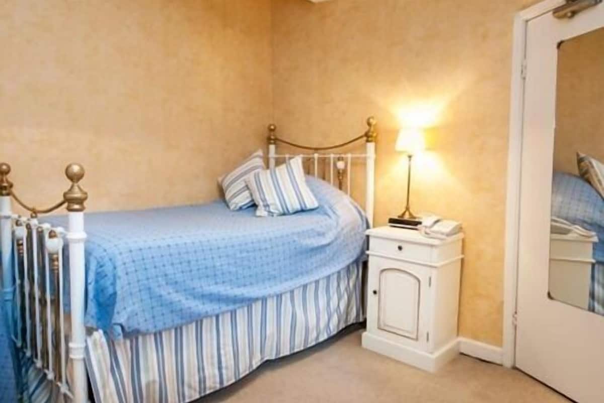 A bedroom with a single bed, a bedside table with a lamp, and a wardrobe.