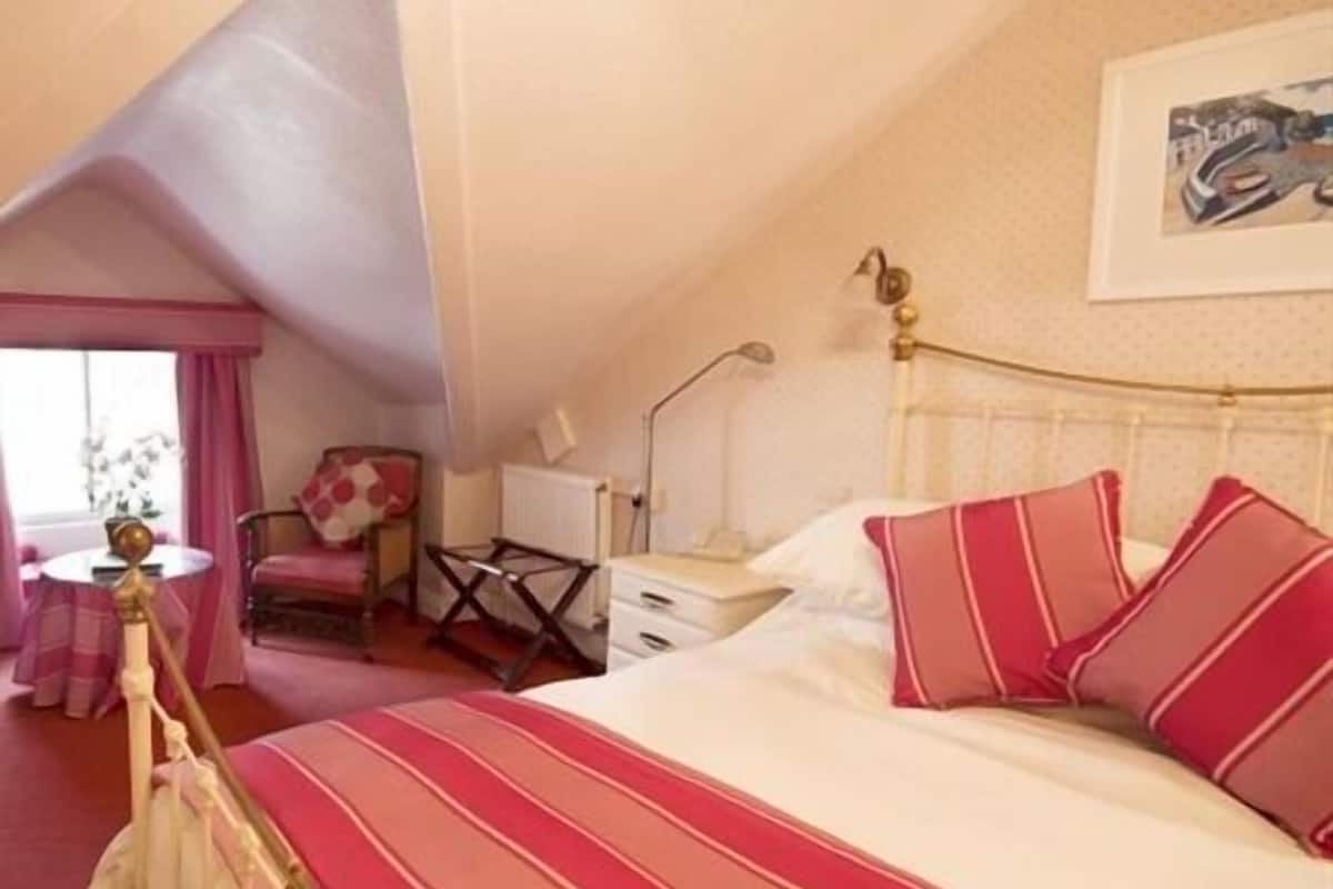 A bedroom with a bed, a chair, a desk, and a window.