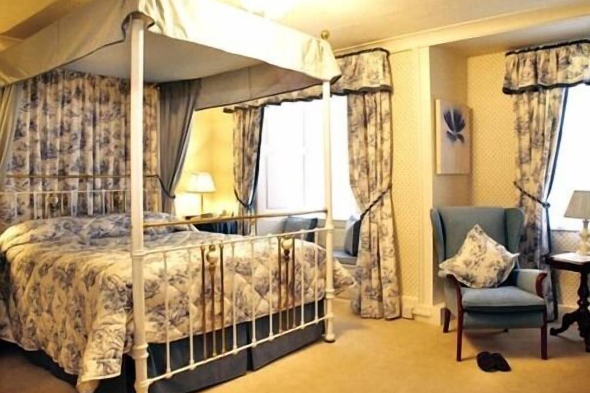 A four-poster bed with a canopy, a chair, and a small table with a lamp.