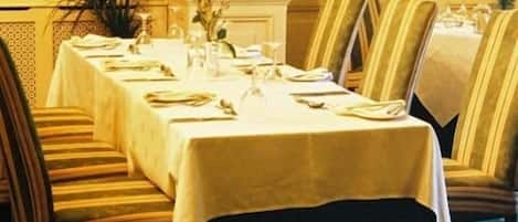 A dining area with a long table set for a meal, striped chairs, and a potted plant.
