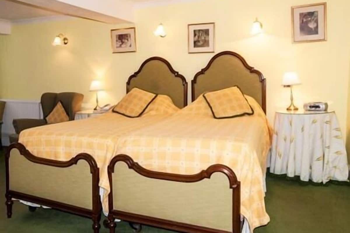 A double bed with a wooden frame and a yellow bedspread, two bedside tables with lamps, and framed pictures on the wall.