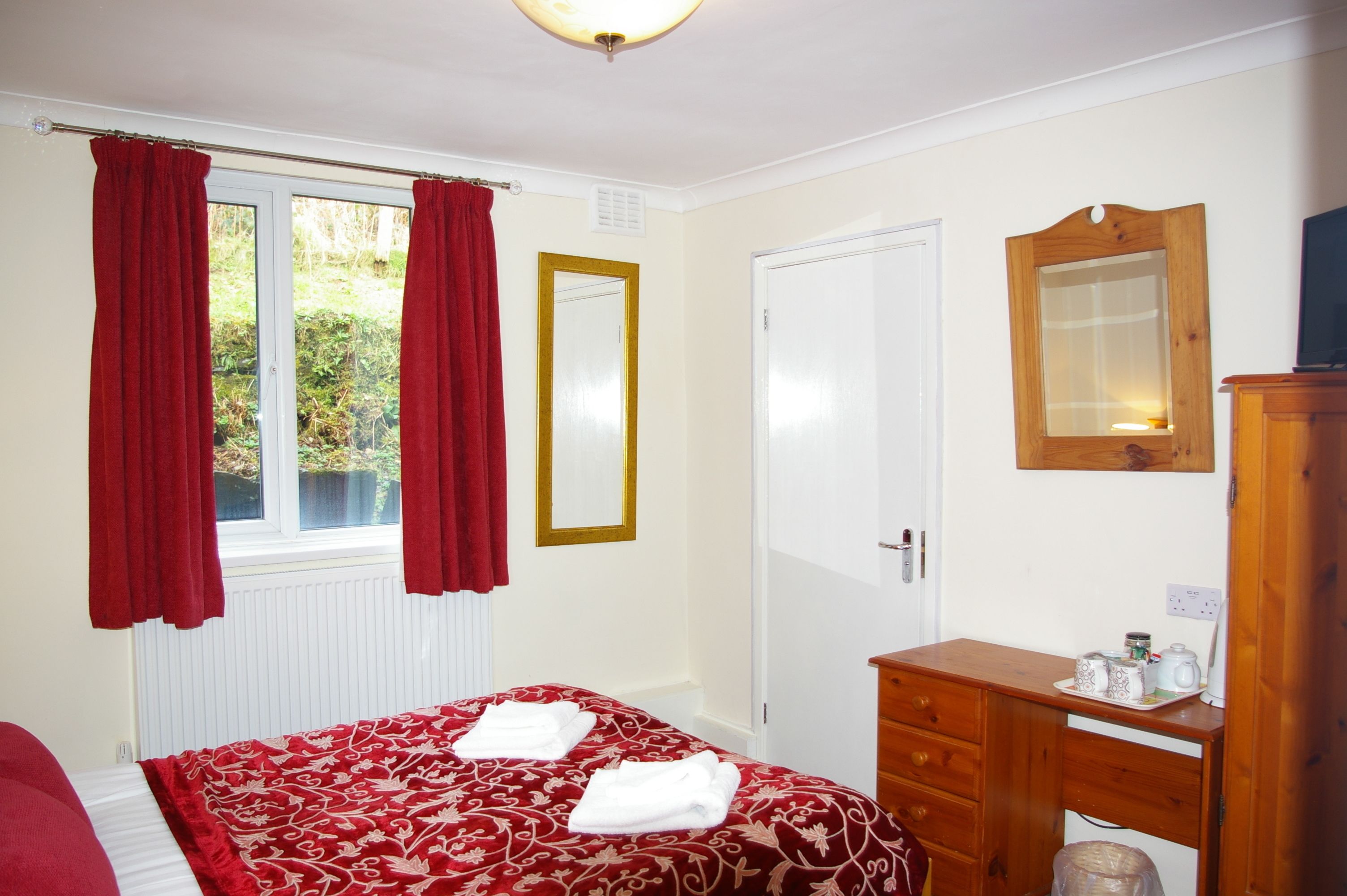 A bedroom with a bed, a wooden dresser, a mirror, and a window with curtains.