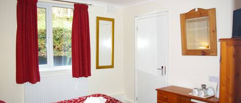 A bedroom with a bed, a wooden dresser, a mirror, and a window with curtains.