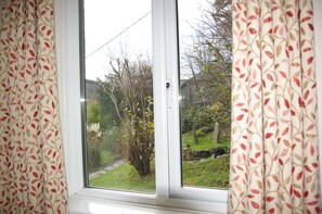 A window with a view of a garden, curtains with a leaf pattern, and a white window frame. - Elen's Castle Hotel (Dolwyddelan)