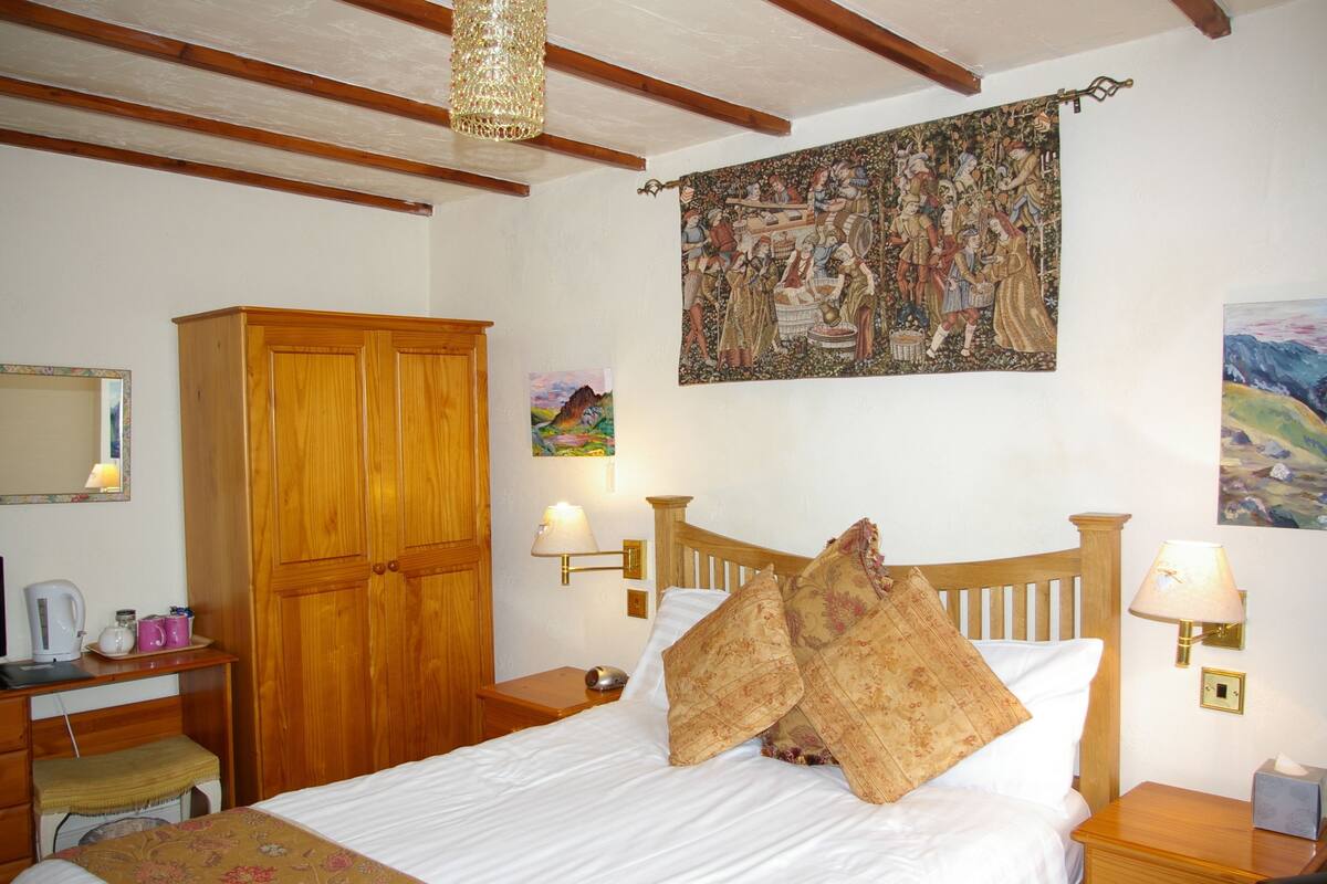 Un dormitorio con una cama de madera, un armario de madera, un escritorio con lámpara y un tapiz en la pared.