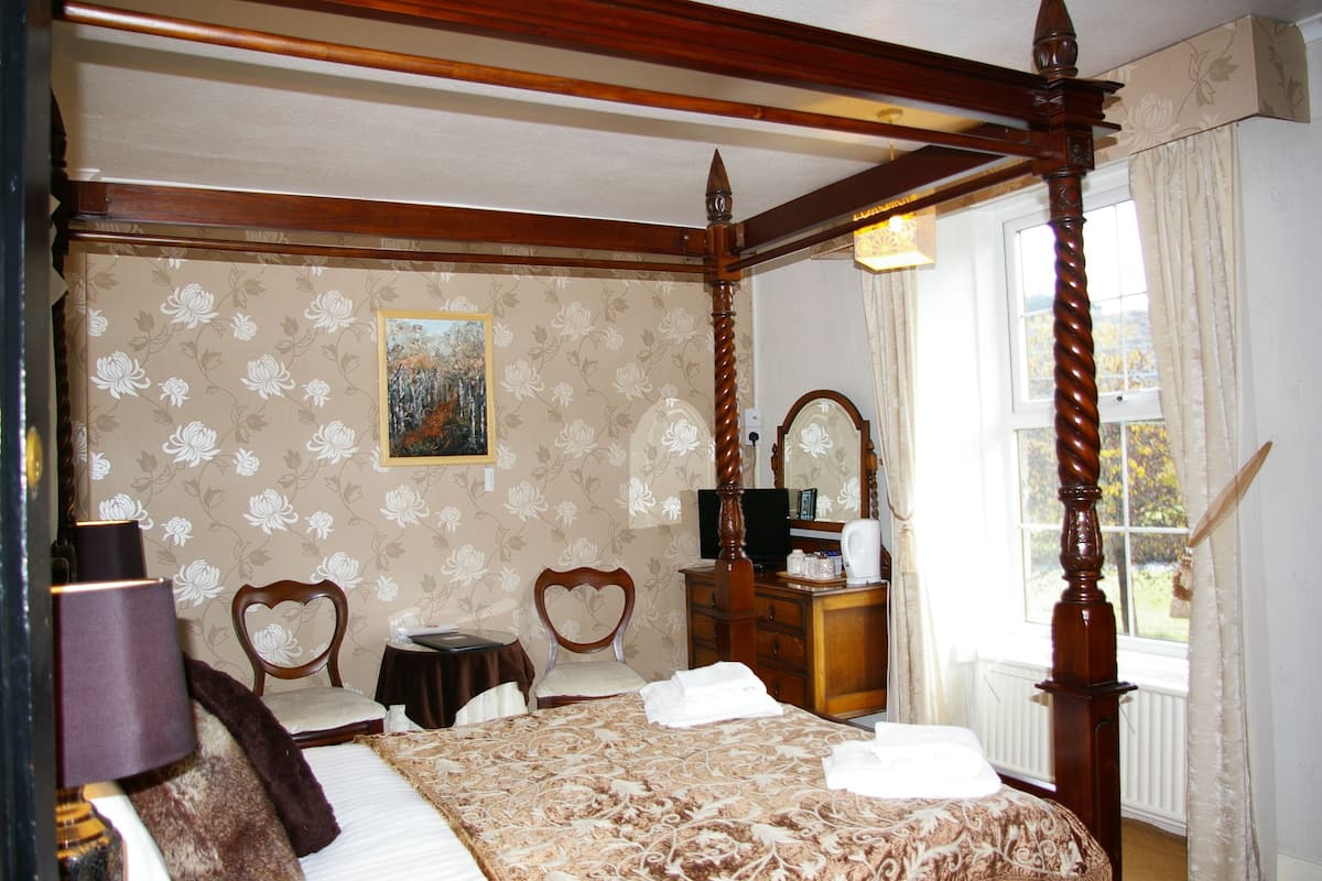 Un dormitorio tradicional con una cama con dosel, un aparador de madera, una silla y una mesita.