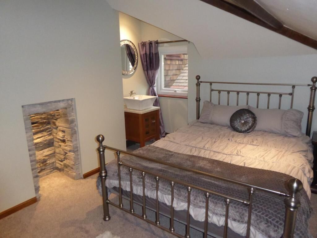 Een slaapkamer met een bed, nachtkastje, spiegel en een stenen muur.