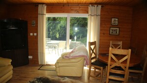 Ein Holzinterieur mit einer Couch, einem Ledersessel, einem Esstisch mit Stühlen und einem Fernseher.