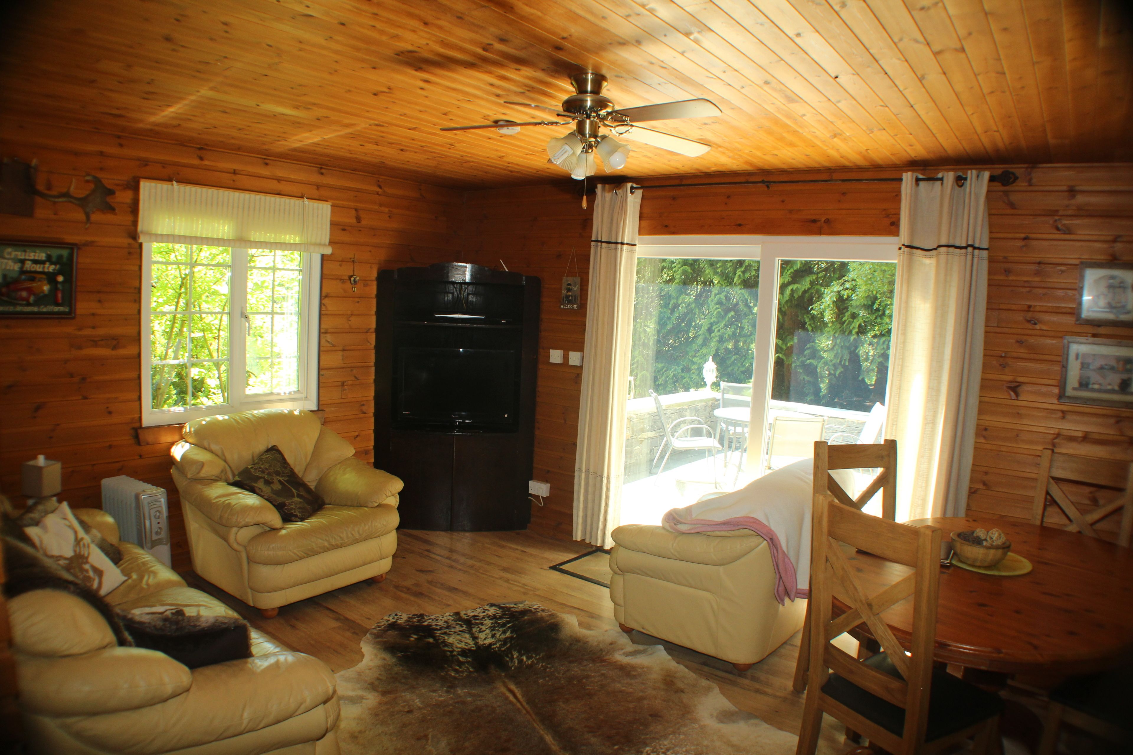 Ein gemütliches Blockhaus-Interieur mit Holzwänden, einem Deckenventilator, einem Kamin und einer Essecke mit Tisch und Stühlen.