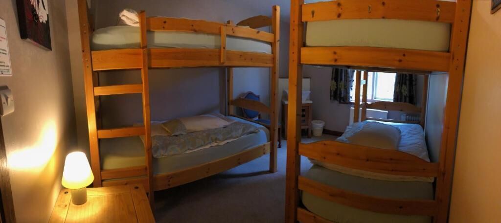 A bunk bed room with a wooden ladder, a bedside table with a lamp, and a window with curtains.