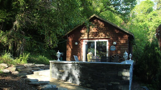Eine rustikale Holzhütte mit Stein Fundament und Holzdach, umgeben von dichtem Wald.