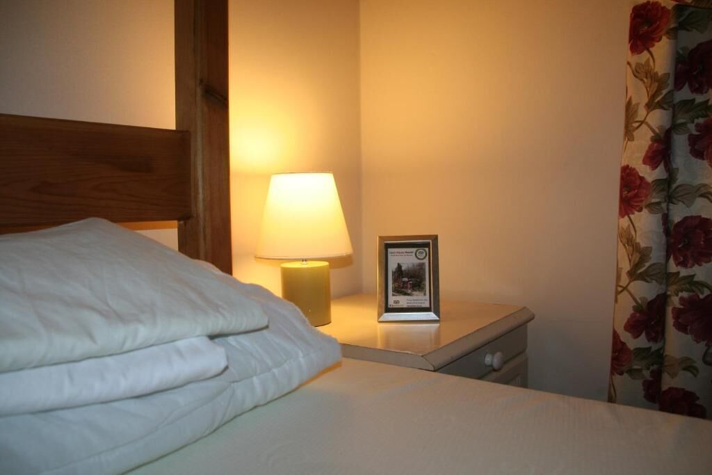 A neatly made bed with a white comforter, a bedside lamp, and a framed picture on a nightstand.