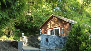 Eine kleine Holzhütte mit Stein Fundament, umgeben von dichtem Wald.