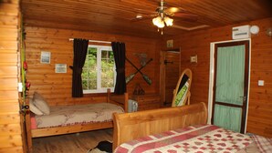 Eine Hütte mit zwei Holzbett, einem Deckenventilator und einem Fenster mit Vorhängen.