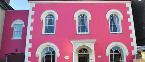 A pink building with white trim, multiple windows, and a central entrance.