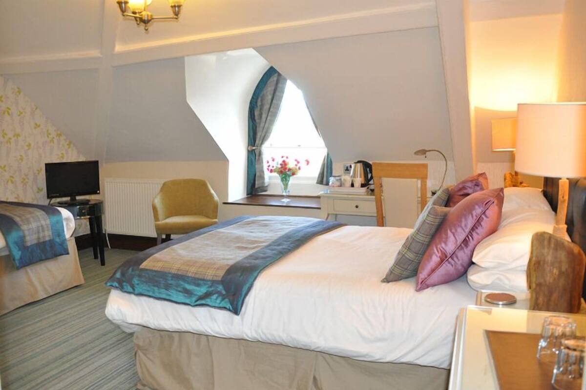 A hotel room with a large bed, a desk with a computer, a chair, a window with curtains, and a lamp.
