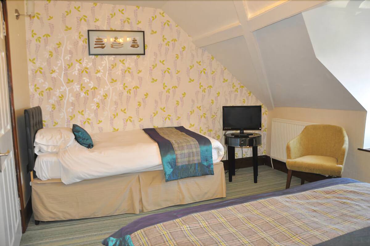 A hotel room with a bed, a chair, a TV, and a radiator.