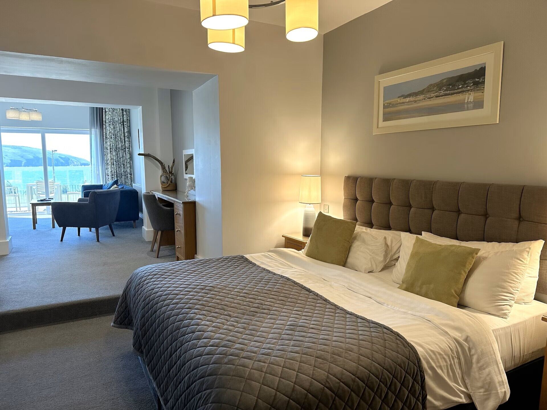 Een hotelkamer met een groot bed, een bureau, een stoel en uitzicht op zee.