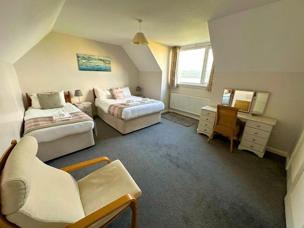 A bedroom with two beds, a desk, a chair, and a window.