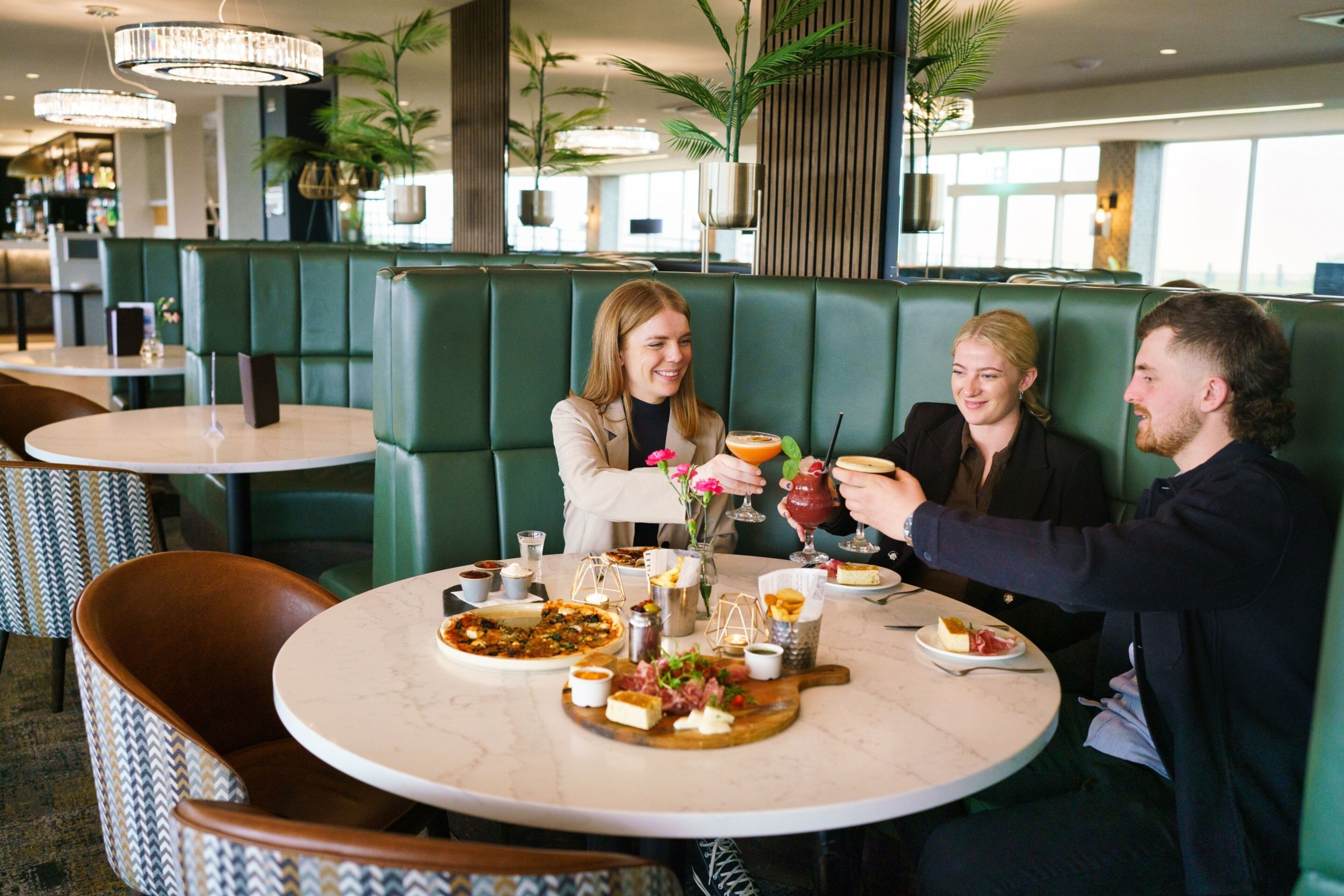 A restaurant with green booths, marble tables, and a variety of dishes and drinks.