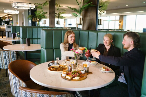 Un restaurante con asientos de color verde, mesas de mármol y una amplia variedad de platos y bebidas.