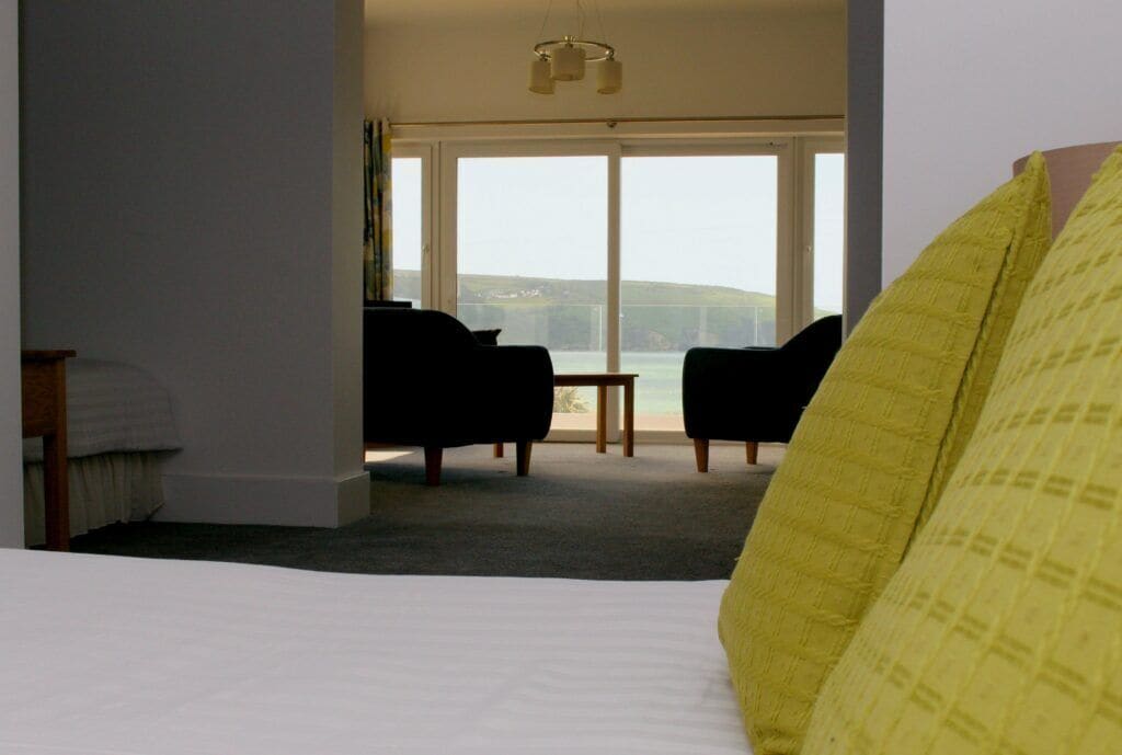 A bedroom with a bed, a window with a view of the beach, and a small table with chairs.