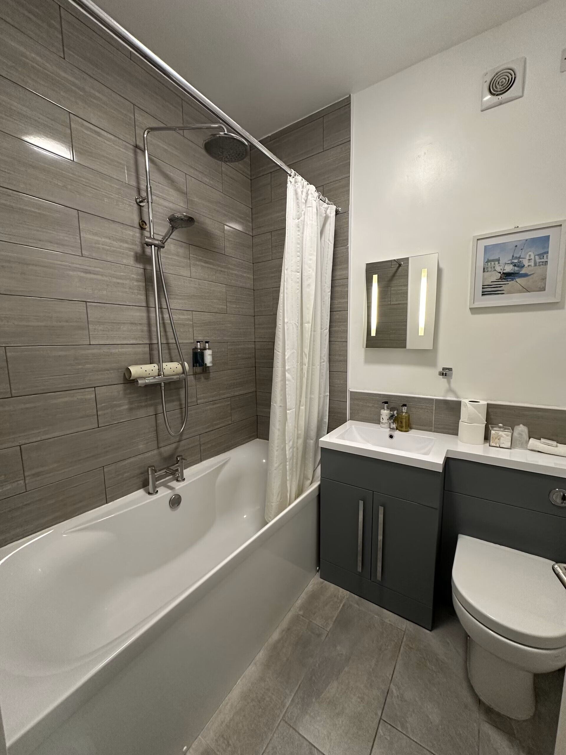 Een moderne badkamer met een vrijstaand bad, douchekop, toilet en een wastafel met spiegel.